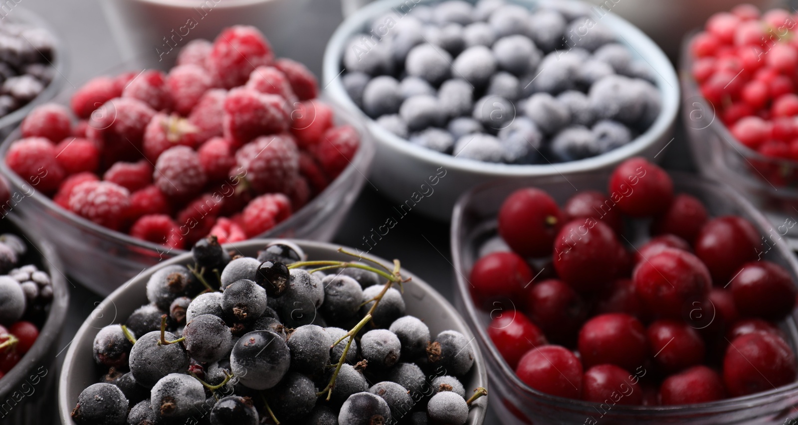 Photo of Different ripe frozen berries in bowls on table, closeup