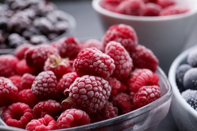 Photo of Different ripe frozen berries in bowls on grey table, closeup