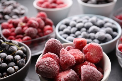Photo of Different ripe frozen berries in bowls on grey table, closeup