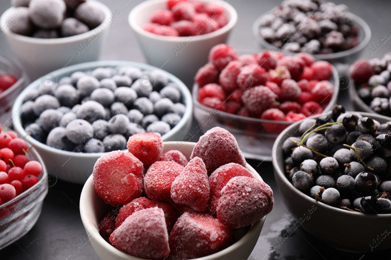 Photo of Different ripe frozen berries in bowls on grey table, closeup