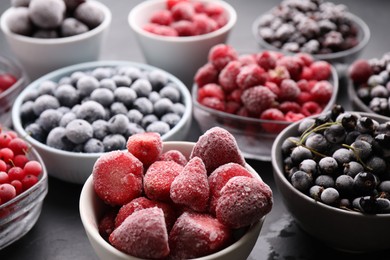 Photo of Different ripe frozen berries in bowls on grey table, closeup