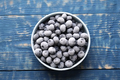 Photo of Ripe frozen blueberries in bowl on blue wooden table, top view