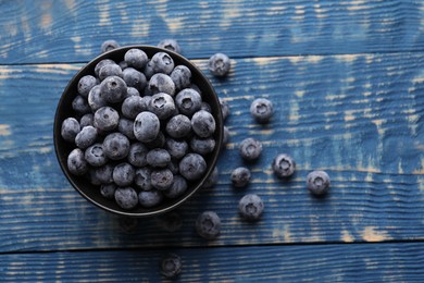 Photo of Ripe frozen blueberries in bowl on blue wooden table, flat lay