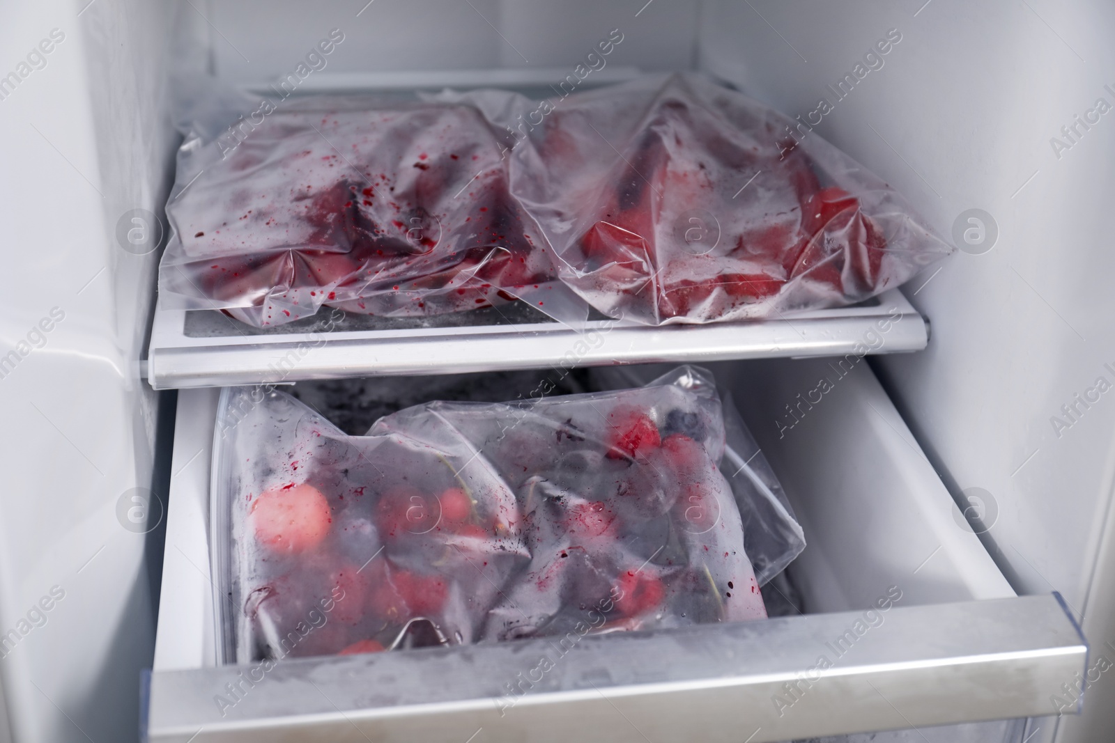 Photo of Different frozen berries in plastic bags in open fridge