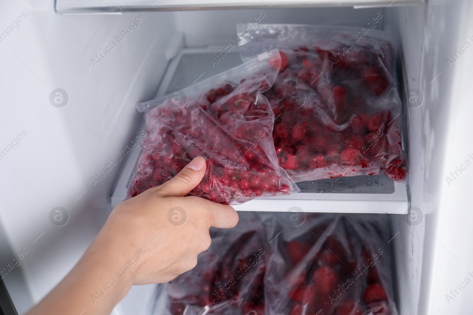 Photo of Woman taking plastic bag with frozen red currants out of fridge, closeup