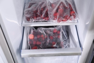 Photo of Different frozen berries in plastic bags in open fridge
