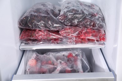 Photo of Different frozen berries in plastic bags in open fridge
