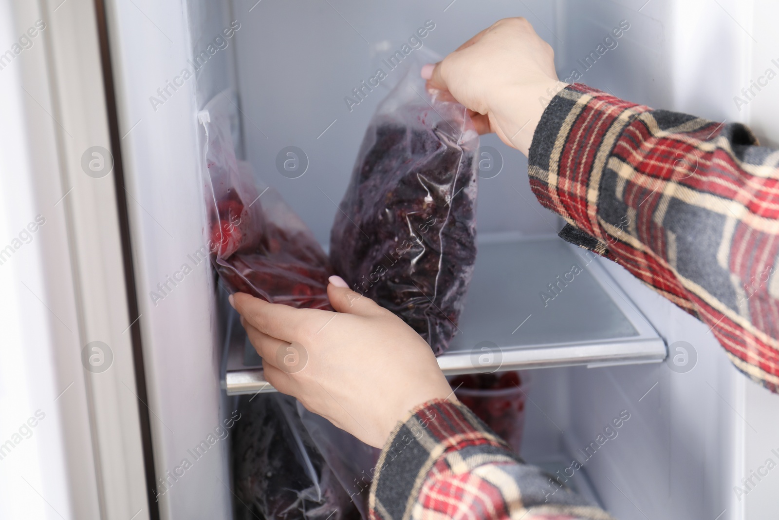 Photo of Woman taking plastic bags with frozen berries out of fridge, closeup