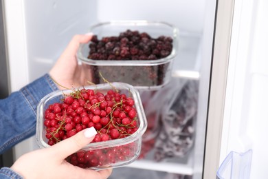 Photo of Freezing berries. Woman putting containers with berries into open fridge, closeup