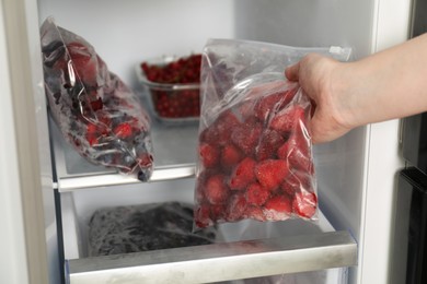 Photo of Woman with plastic bag of frozen strawberries near open fridge, closeup