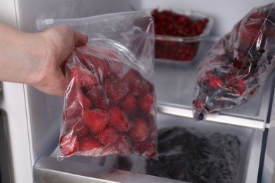 Photo of Woman with plastic bag of frozen strawberries near open fridge, closeup