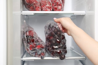 Photo of Woman taking plastic bag with frozen cherries out of fridge, closeup