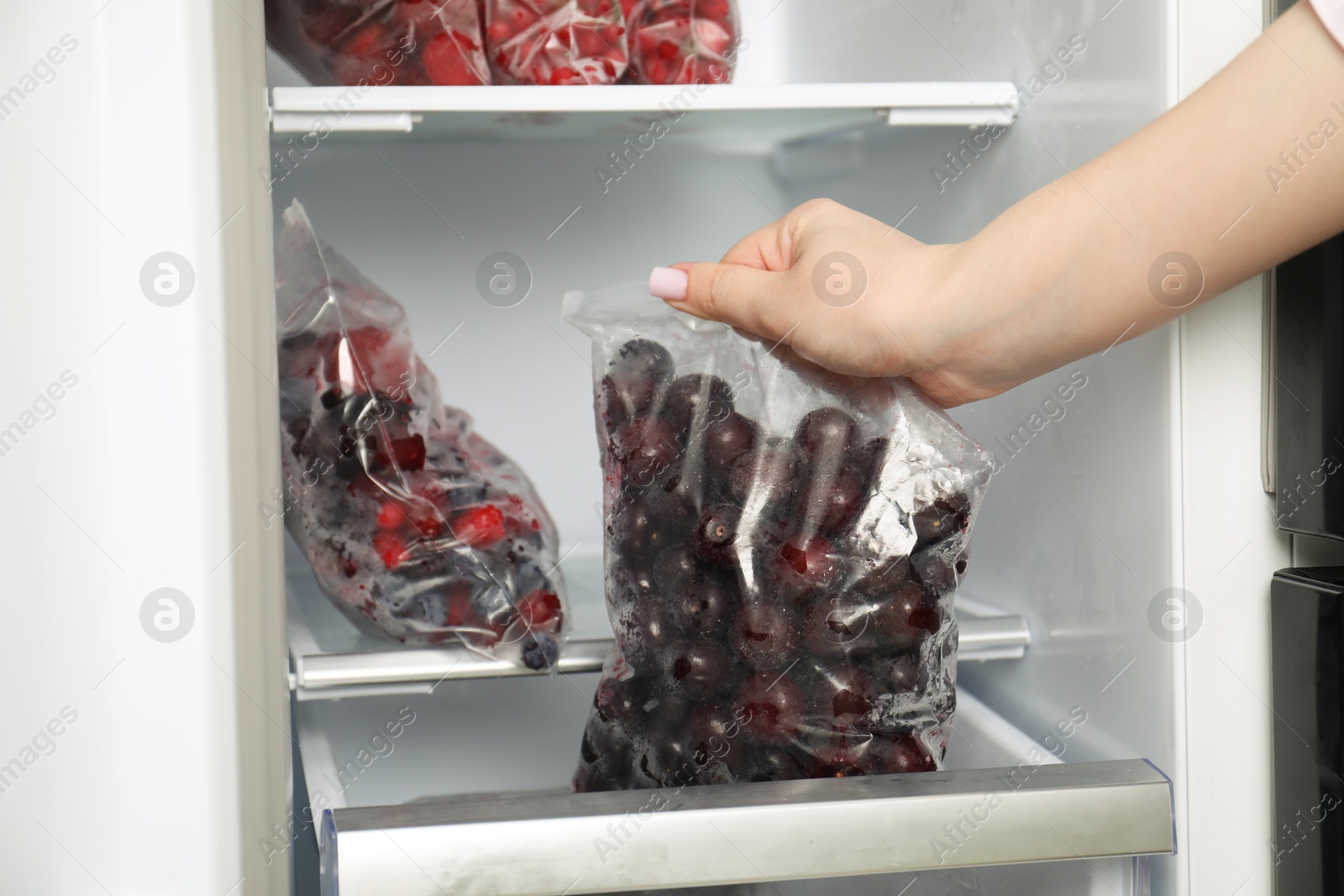 Photo of Woman taking plastic bag with frozen cherries out of fridge, closeup