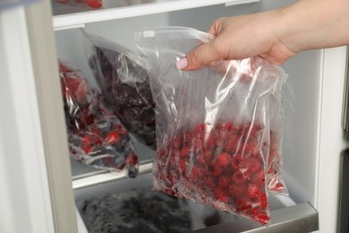 Photo of Woman with plastic bags of frozen berries near open fridge, closeup