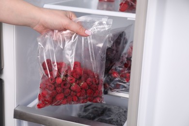 Photo of Freezing berries. Woman putting plastic bag with raspberries into open fridge, closeup