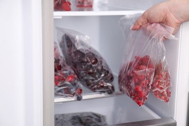 Photo of Woman with plastic bags of frozen berries near open fridge, closeup