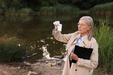 Photo of Forensic expertise. Detective with clipboard and evidence at crime scene near lake outdoors, space for text
