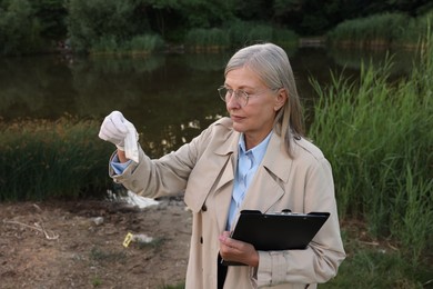 Photo of Forensic expertise. Detective with clipboard and evidence at crime scene near lake outdoors