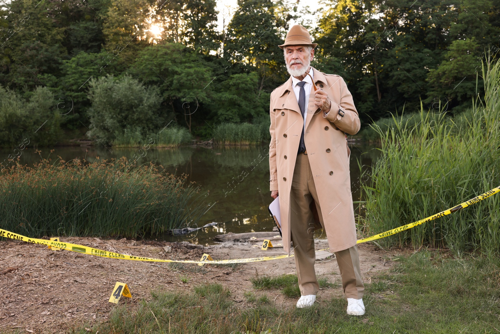 Photo of Forensic expertise. Detective with smoking pipe and clipboard working at crime scene near lake outdoors, space for text