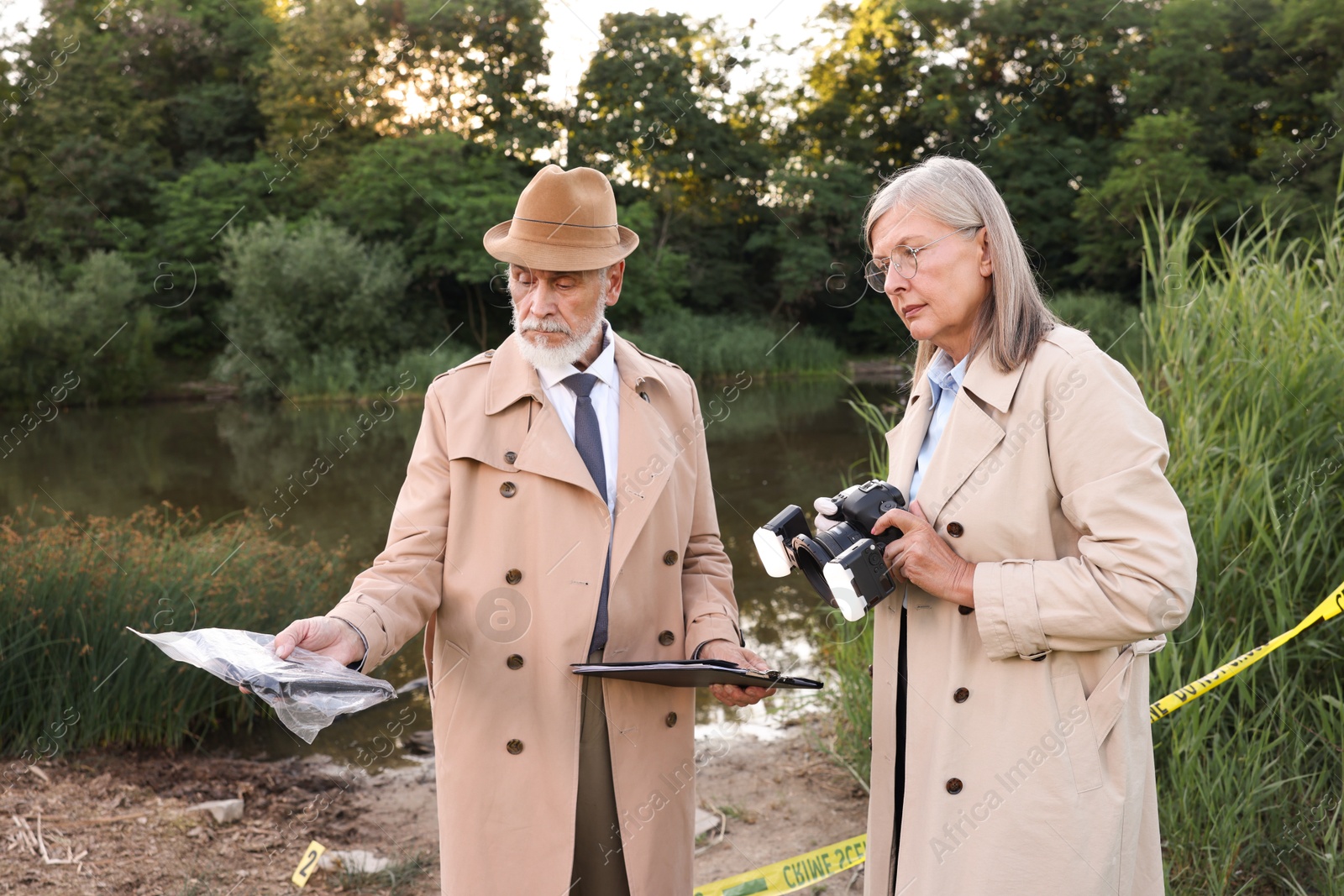 Photo of Forensic expertise. Detectives working at crime scene near lake outdoors