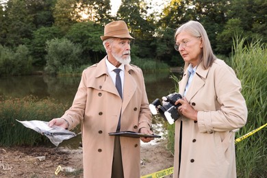 Photo of Forensic expertise. Detectives working at crime scene near lake outdoors