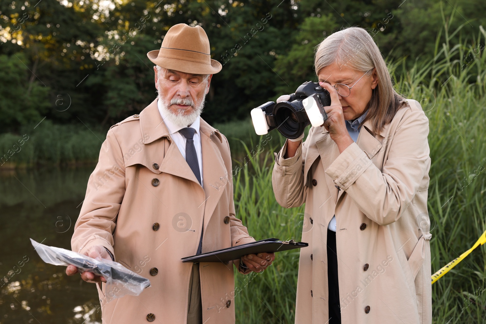 Photo of Forensic expertise. Detectives working at crime scene near lake outdoors