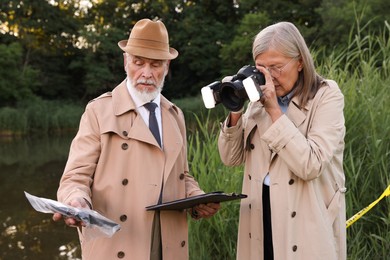 Photo of Forensic expertise. Detectives working at crime scene near lake outdoors