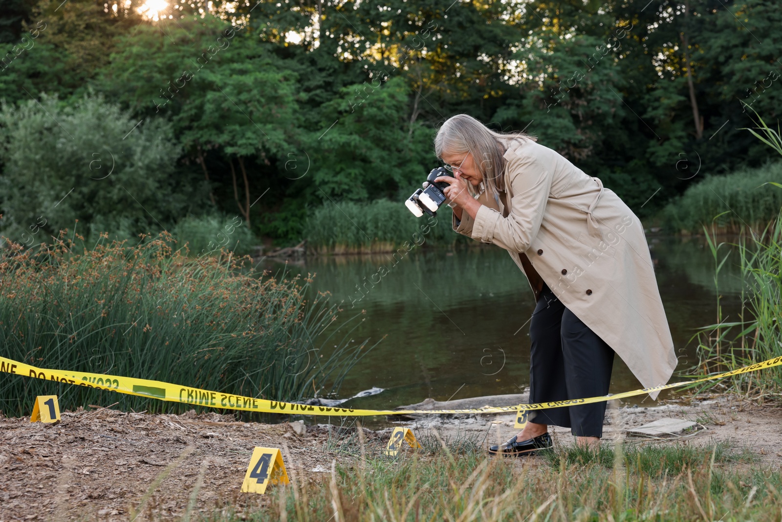 Photo of Forensic expertise. Detective with camera working at crime scene near lake outdoors, space for text