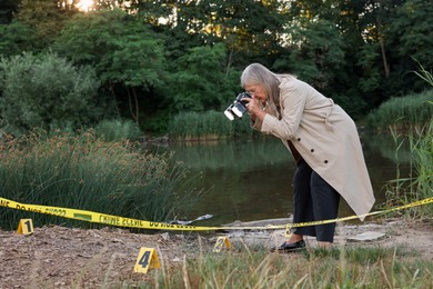 Photo of Forensic expertise. Detective with camera working at crime scene near lake outdoors, space for text