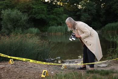 Photo of Forensic expertise. Detective with camera working at crime scene near lake outdoors, space for text