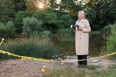 Photo of Forensic expertise. Detective with camera working at crime scene near lake outdoors, space for text