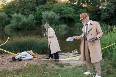 Photo of Forensic expertise. Detectives working at crime scene with dead man's body near lake outdoors