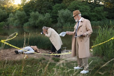 Photo of Forensic expertise. Detectives working at crime scene with dead man's body near lake outdoors