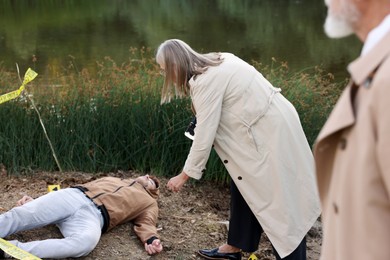 Photo of Forensic expertise. Detectives working at crime scene with dead man's body near lake outdoors