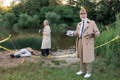 Photo of Forensic expertise. Detectives working at crime scene with dead man's body near lake outdoors