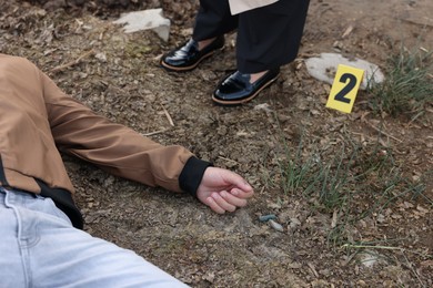 Photo of Forensic expertise. Detective near dead man's body at crime scene outdoors, closeup