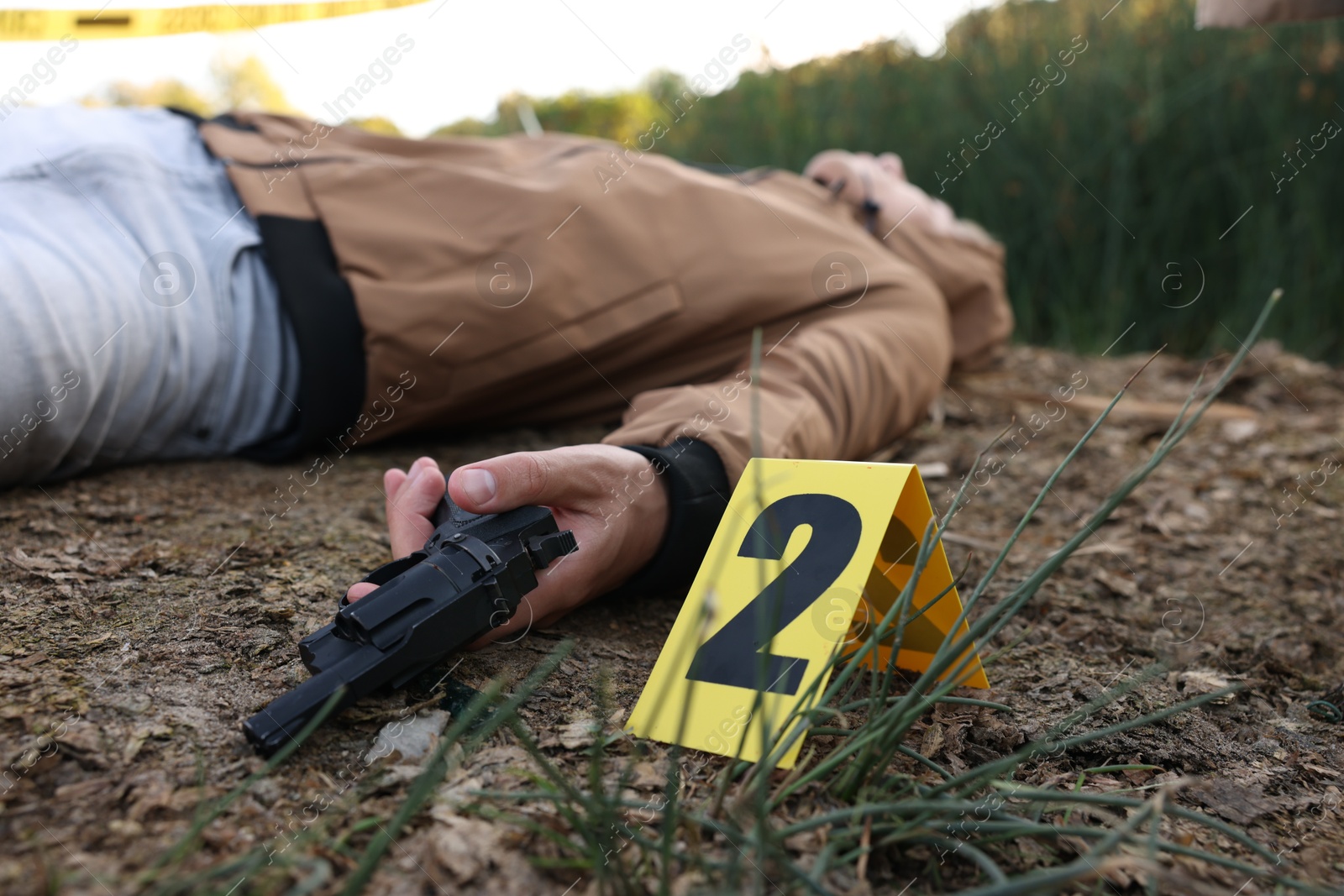 Photo of Forensic expertise. Crime scene with dead man's body, gun and marker outdoors, selective focus