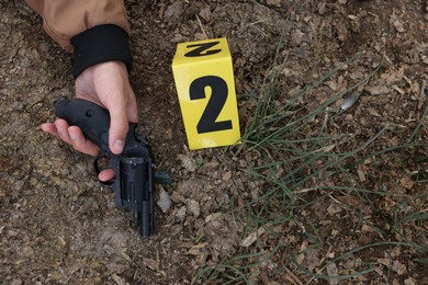 Photo of Forensic expertise. Crime scene with dead man's body, gun and marker outdoors, top view