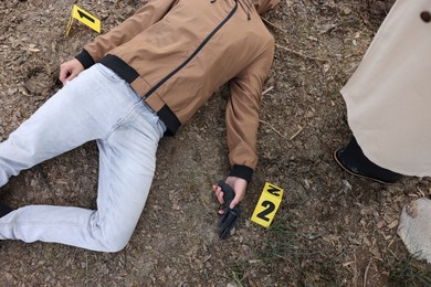 Photo of Forensic expertise. Detective near dead man's body at crime scene outdoors, top view