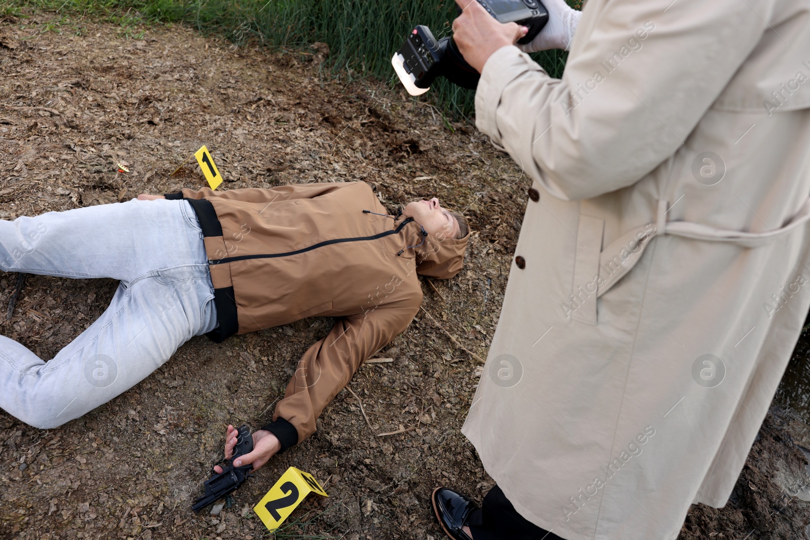 Photo of Forensic expertise. Detective with camera working at crime scene with dead man's body outdoors, above view