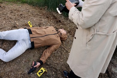 Photo of Forensic expertise. Detective with camera working at crime scene with dead man's body outdoors, above view