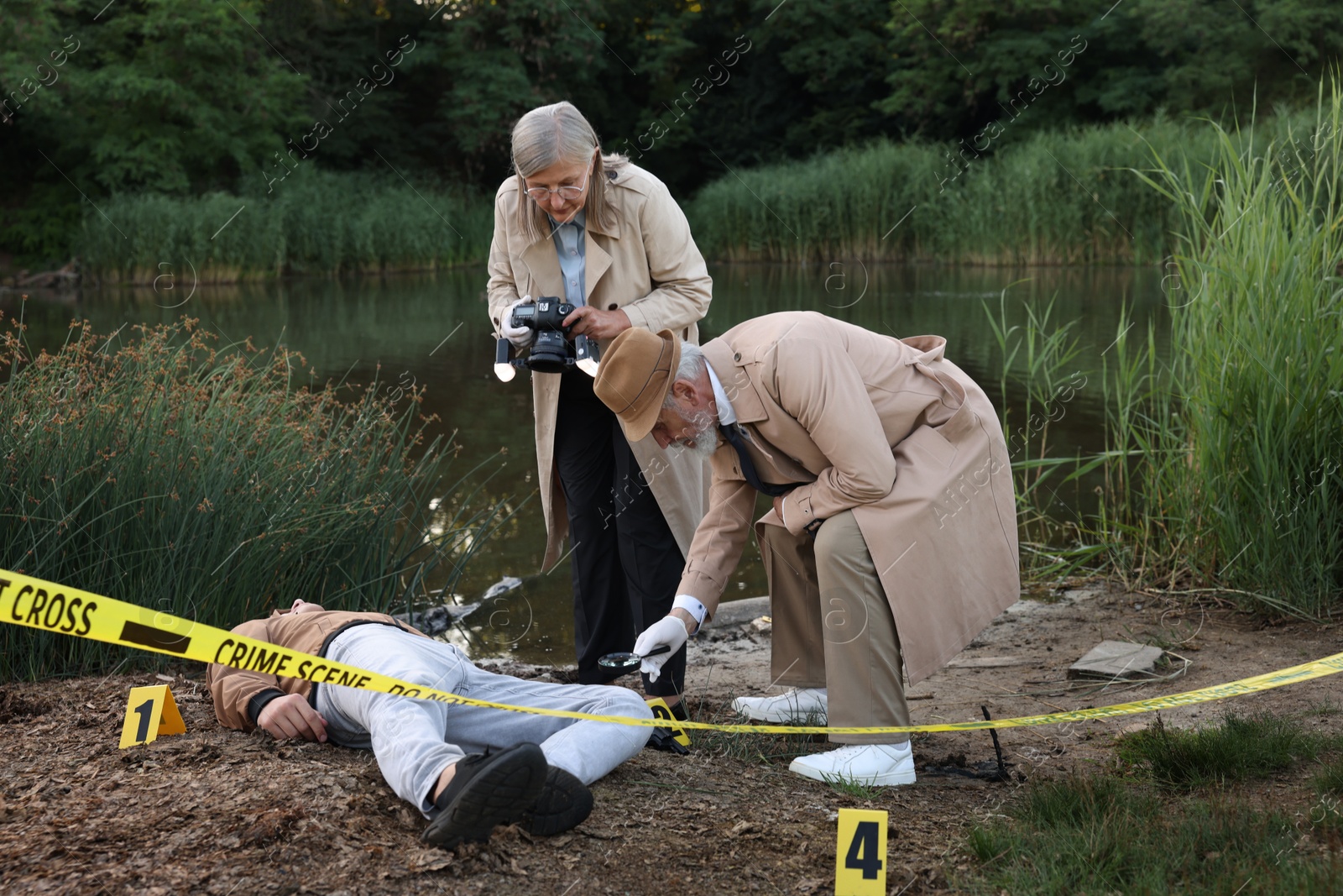 Photo of Forensic expertise. Detectives working at crime scene with dead man's body near lake outdoors