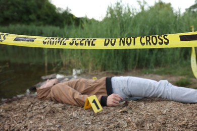 Photo of Forensic expertise. Crime scene with dead man's body and marker near lake outdoors, selective focus