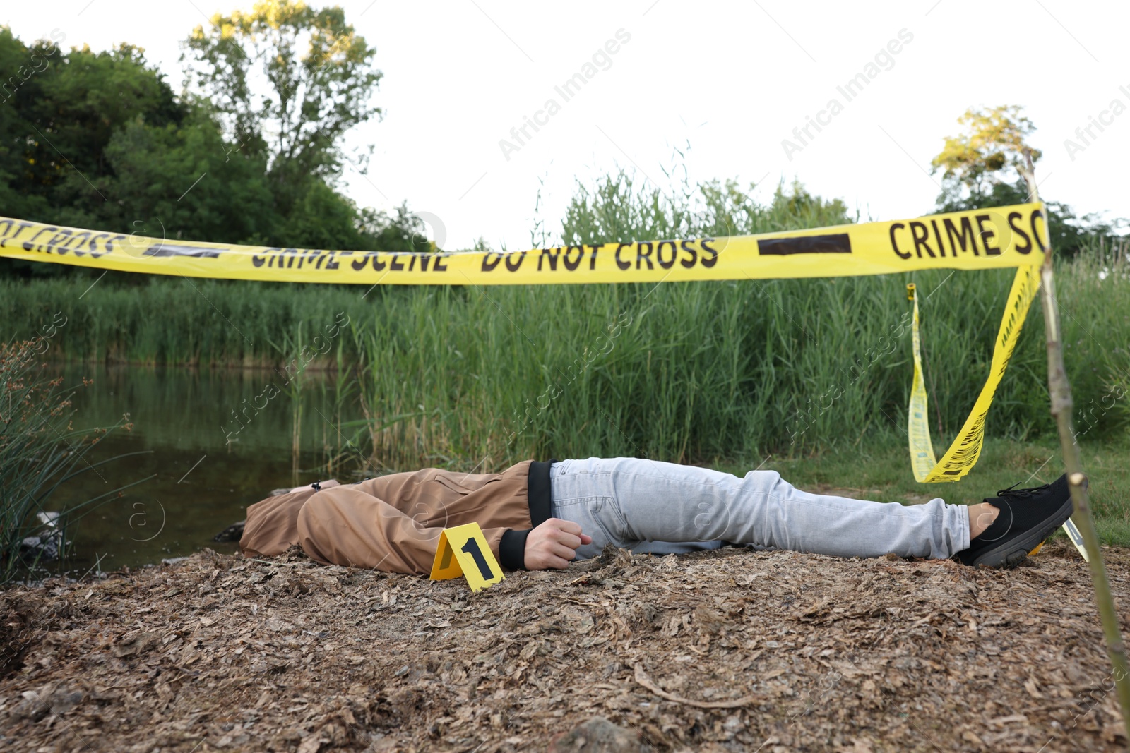 Photo of Forensic expertise. Crime scene with dead man's body and marker near lake outdoors