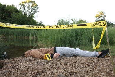 Photo of Forensic expertise. Crime scene with dead man's body and marker near lake outdoors