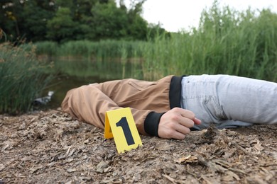 Photo of Forensic expertise. Crime scene with dead man's body and marker near lake outdoors, closeup