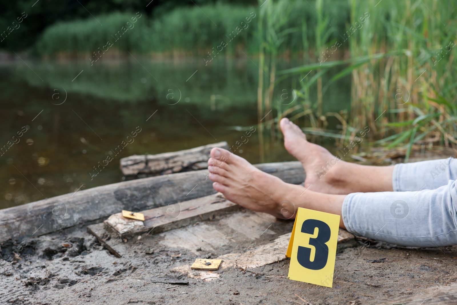 Photo of Forensic expertise. Crime scene with dead man's body and marker near lake outdoors, closeup. Space for text