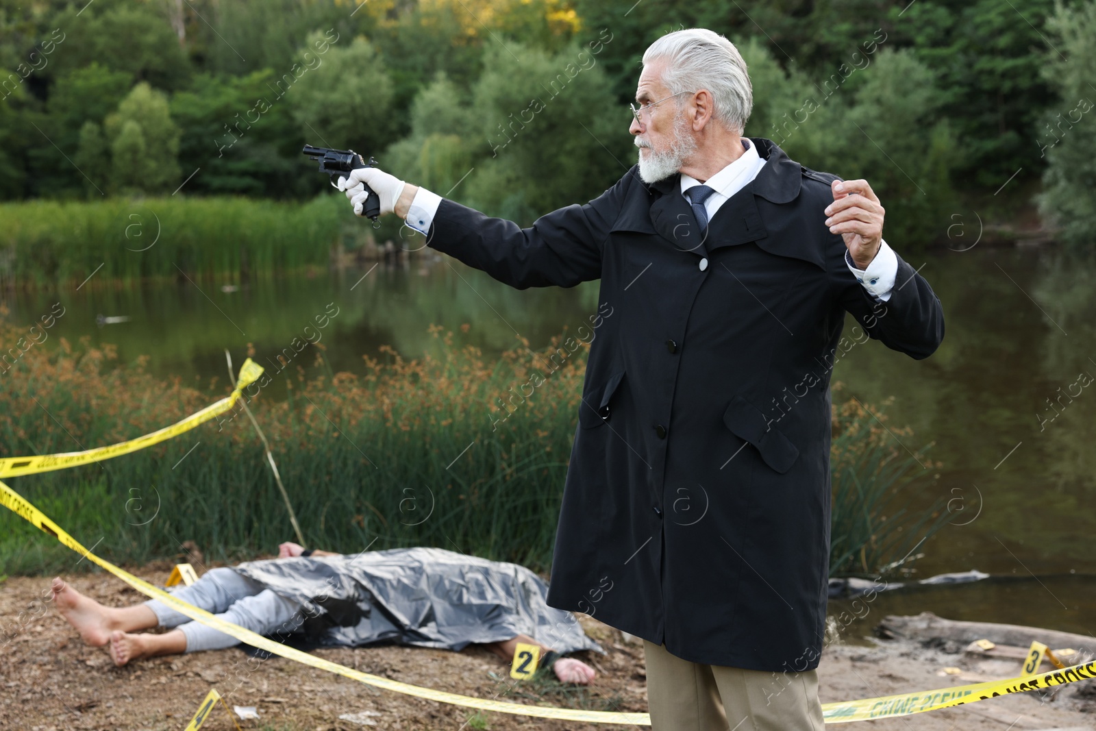 Photo of Forensic expertise. Detective with evidence working at crime scene with dead man's body near lake outdoors