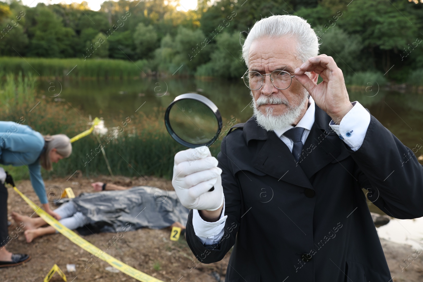 Photo of Forensic expertise. Detectives working at crime scene with dead man's body near lake outdoors, selective focus