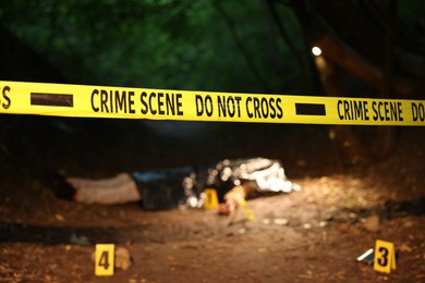 Photo of Forensic expertise. Crime scene with dead man's body and markers outdoors, focus on police tape